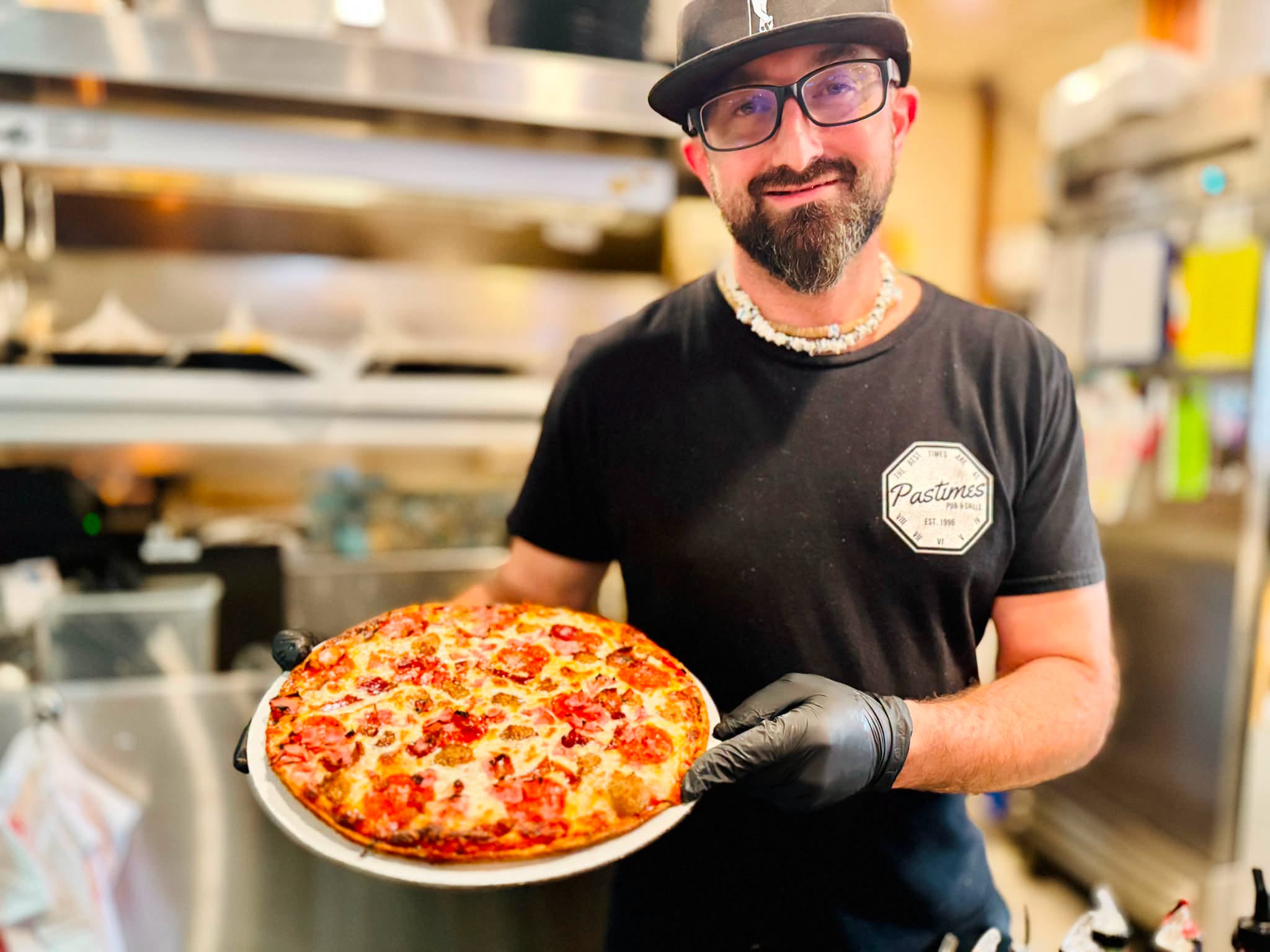 Adam holding a homemade pizza in the Pastimes kitchen